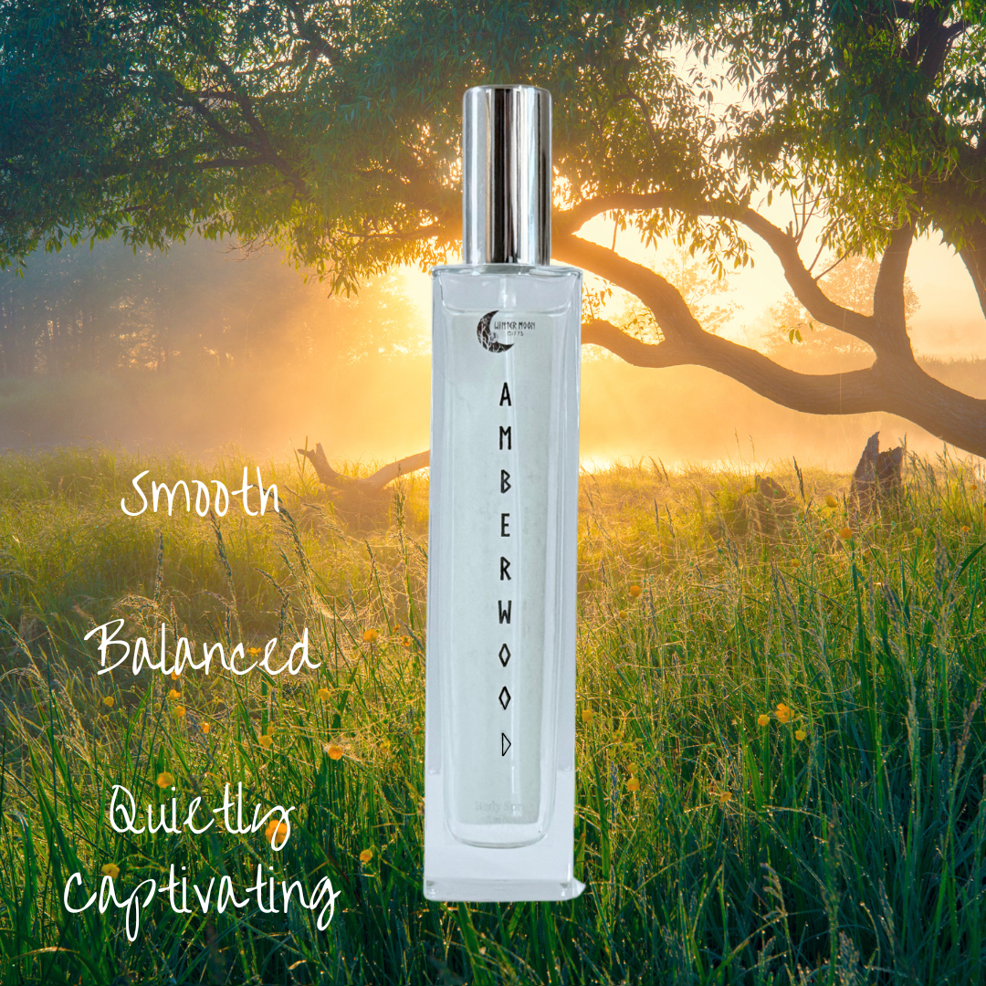 Amberwood body spray bottle standing in a grassy field at sunrise, with trees and golden light in the background. A smooth, balanced, and captivating vibe.