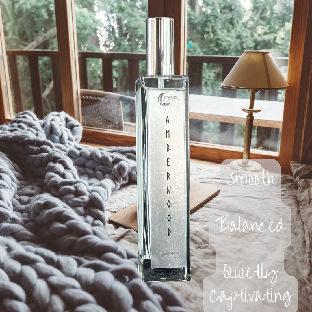 Amberwood room spray bottle in a warm bedroom setting, with text reading “Smooth, Balanced, Quietly Captivating” to reflect the mood of the scent.