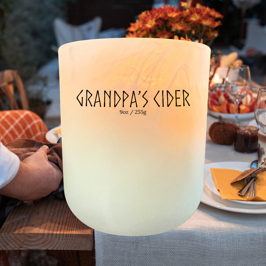 Grandpa’s Cider soy candle on holiday table with pumpkins, fall flowers, and cozy autumn dinner setting