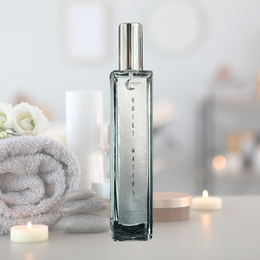 Quiet Waters Room Spray bottle styled with a spa-inspired background including a rolled towel, stacked stones, and soft candlelight